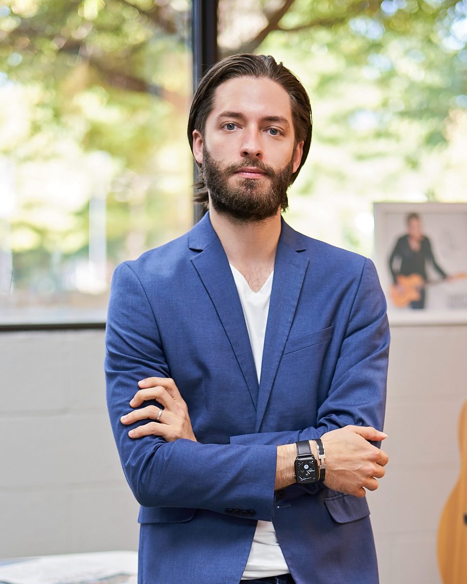 Brian Larsen in a blue blazer, arms crossed, standing by a window in his office